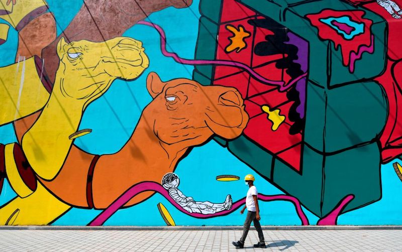 TOPSHOT - A worker wearing a hard hat walks past a mural in Dubai on June 3, 2020. - Shopping malls in Dubai will fully reopen for business on June 3, in the latest easing of COVID-19 coronavirus restrictions, the emirate's media office announced. The step makes the glitzy city-state the first in the Middle East to drop nearly all restrictions to combat the spread of the novel coronavirus that hit retailers and leisure activities. (Photo by Karim SAHIB / AFP) (Photo by KARIM SAHIB/AFP via Getty Images)